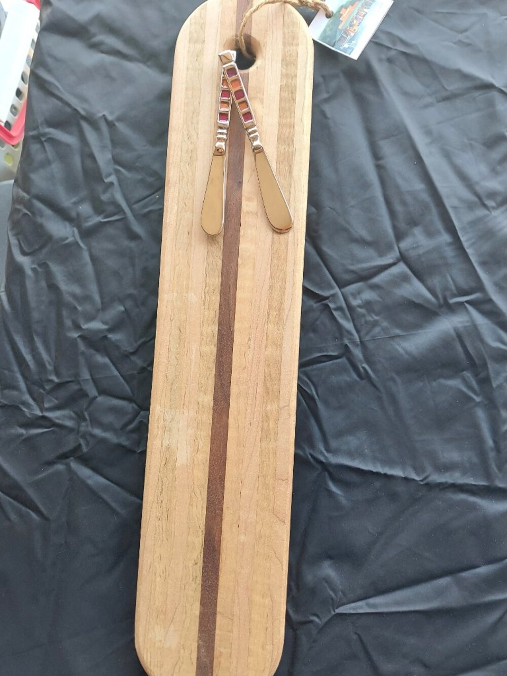 Oval wooden cutting board with 2 colorful cheese knives. 19 inches long